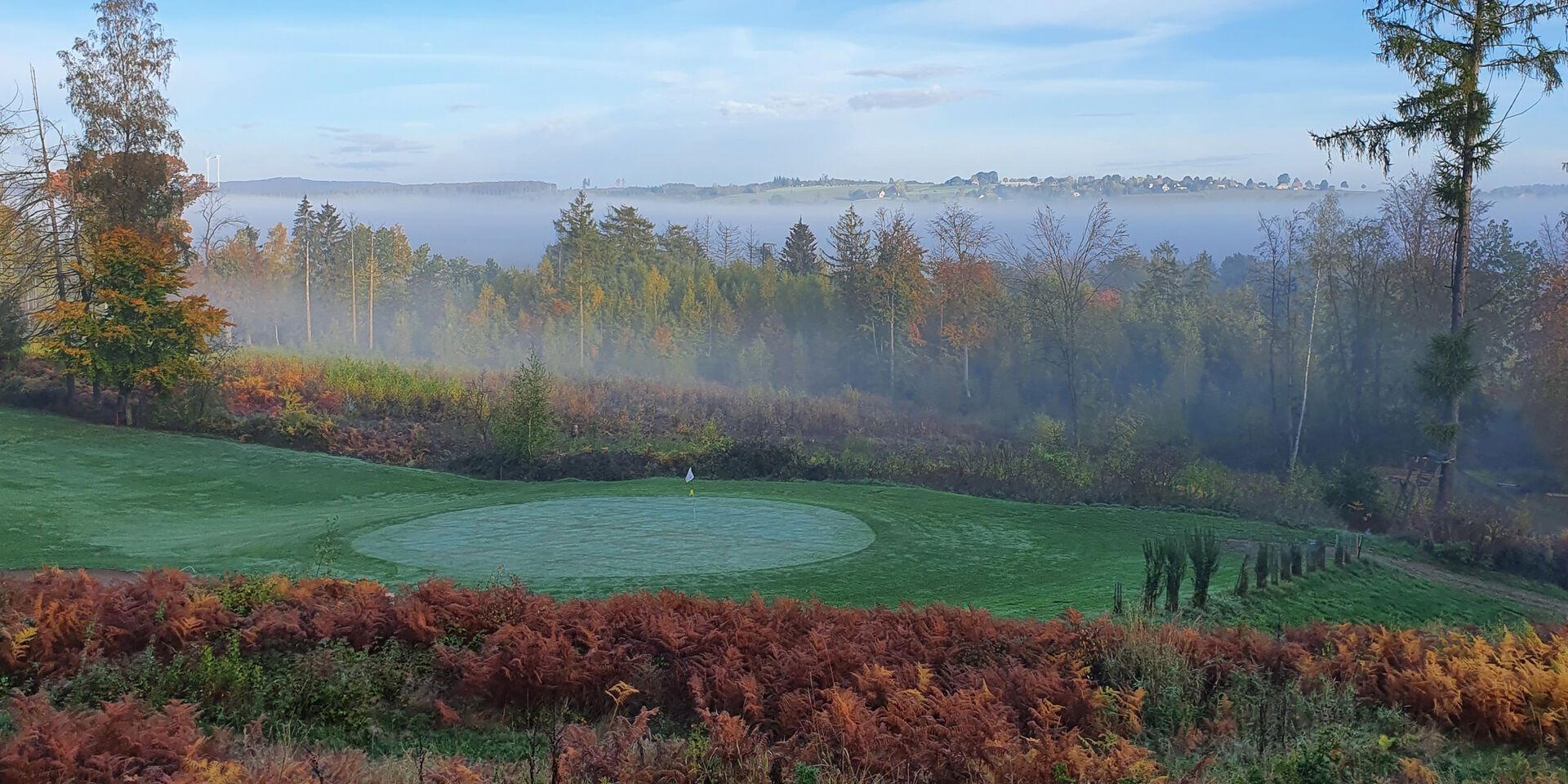 Blick auf ein Grün des BvM-Platzes in Schwöbber, umgeben von Bäumen und leichtem Nebel.